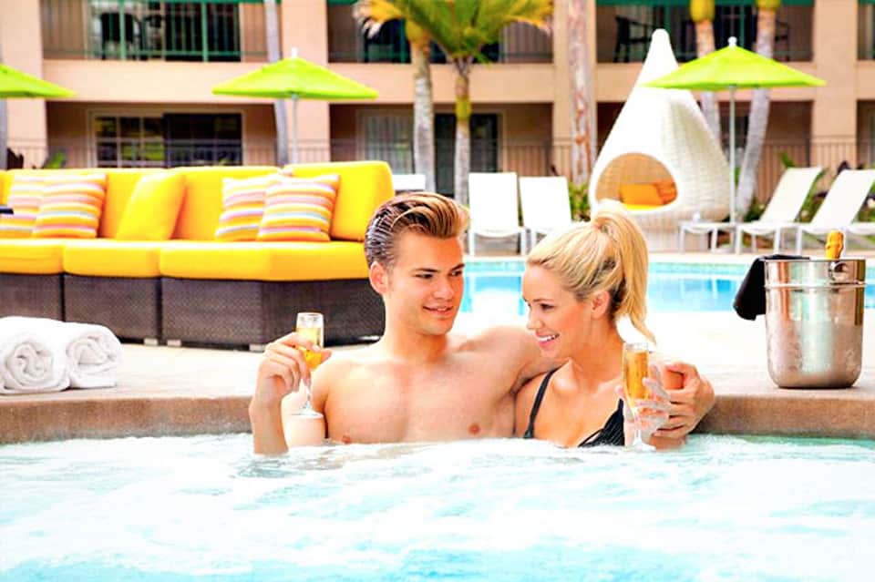 Couple enjoying drinks in hotel hot tub with poolside lounge area in background