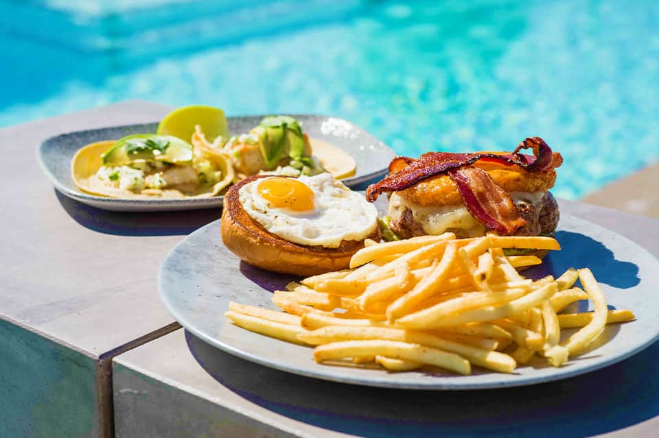 Egg and bacon sandwich with crispy fries served poolside by turquoise water