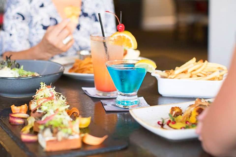 Colorful cocktails and appetizers on a restaurant table with diners in background