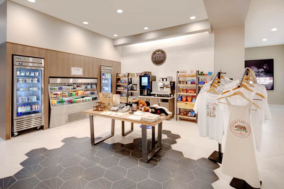 Modern retail shop interior with white walls, wooden shelving, beverage coolers, and branded merchandise on display