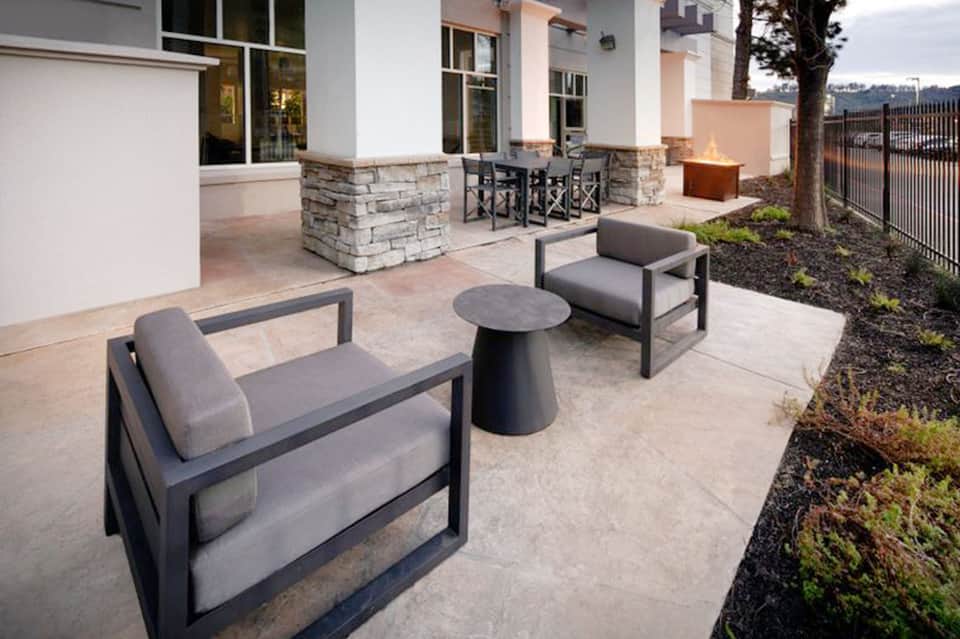 Outdoor patio seating with modern gray lounge chairs, fire pit, and stone accent wall