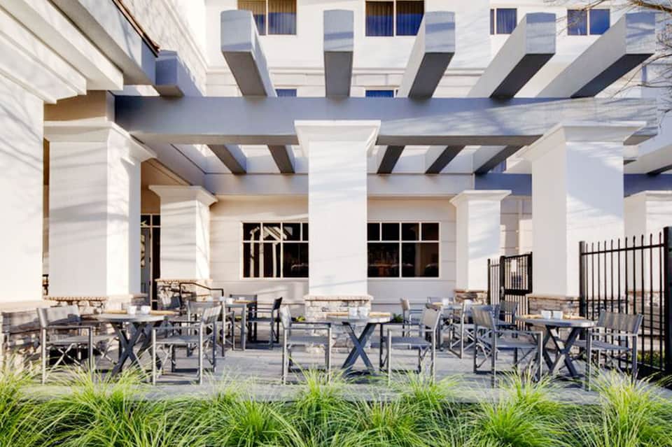 Modern white pergola patio with dining tables, lounge chairs, and manicured landscaping overlooking resort grounds