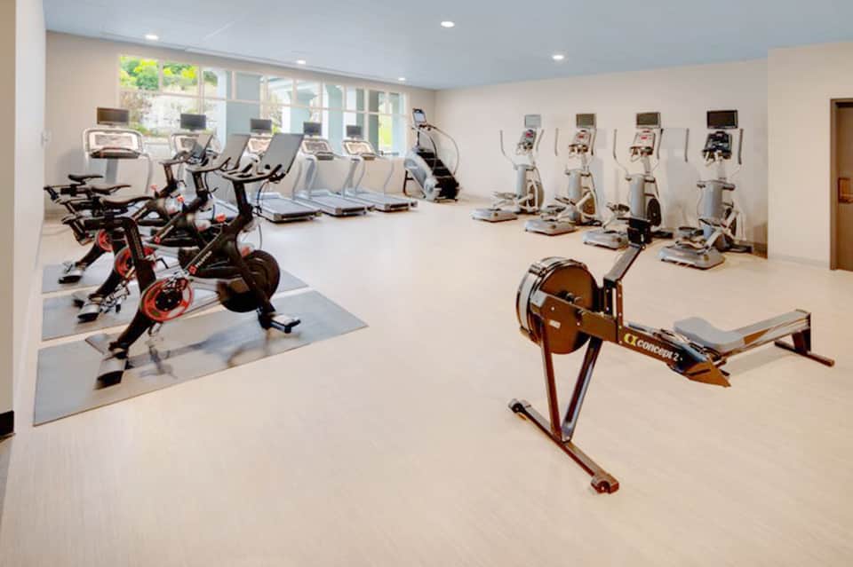 Fitness center with stationary bikes, rowing machine, cardio equipment, and large windows
