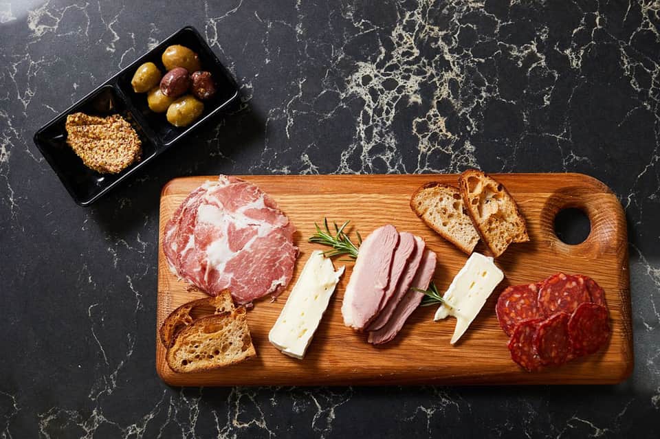 Charcuterie board with cured meats, cheese, olives, crackers on wooden serving platter
