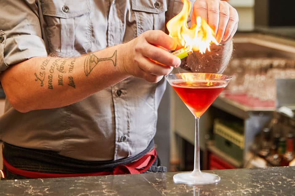 Bartender igniting a flaming cocktail with lime garnish at bar counter