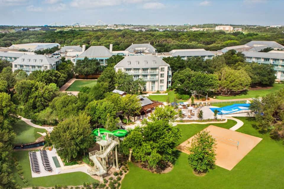 Aerial view of luxury resort with swimming pool, sports courts, and manicured grounds surrounded by trees