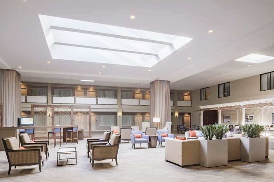 Spacious modern hotel lobby with skylight, seating areas, neutral tones, and contemporary furniture