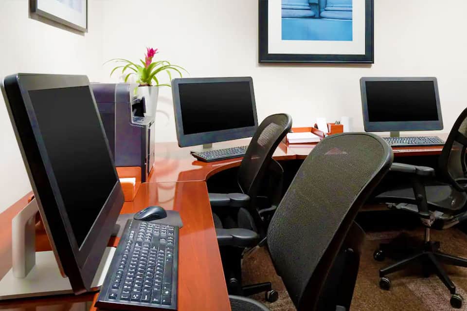 Modern office workspace with orange desks, computer monitors, black chairs, and potted plant