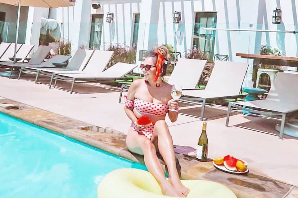 Woman relaxing poolside in polka dot swimsuit with wine and fruit refreshments