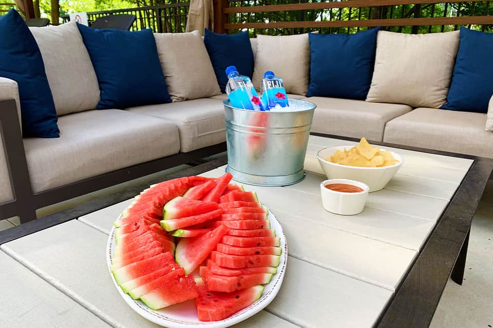 Outdoor patio with beige sectional sofa, watermelon platter, and ice bucket on table