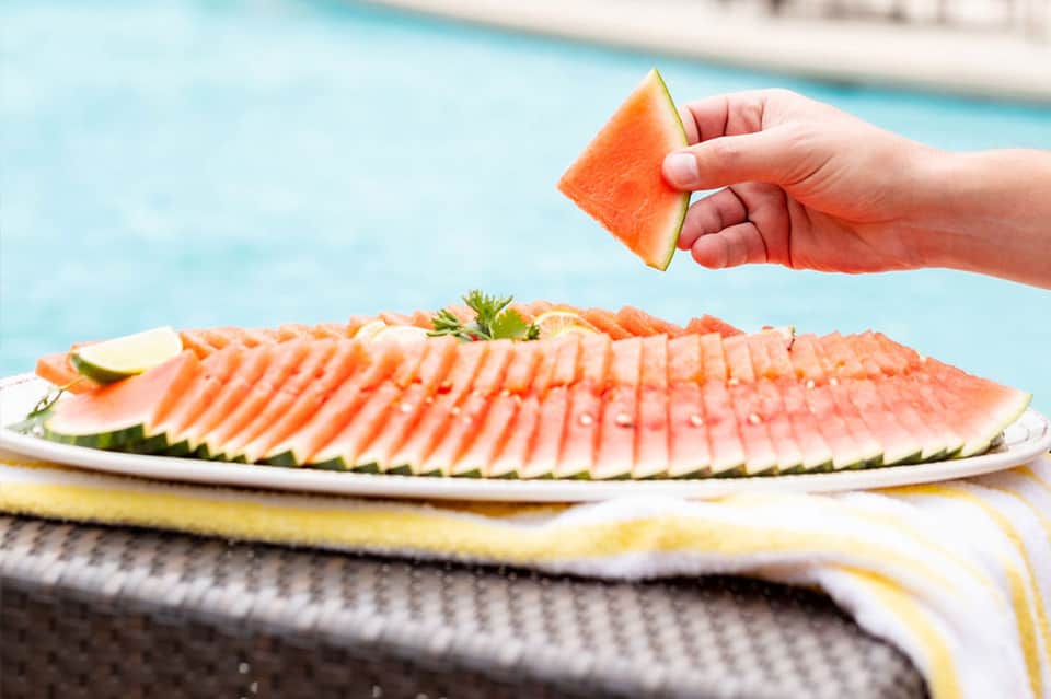 Sliced grapefruit held over plated smoked salmon with citrus garnish by pool