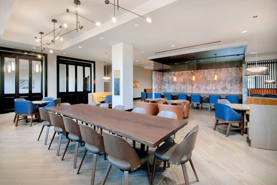 Modern hotel lobby with wooden dining table, blue chairs, pendant lighting, and contemporary furnishings