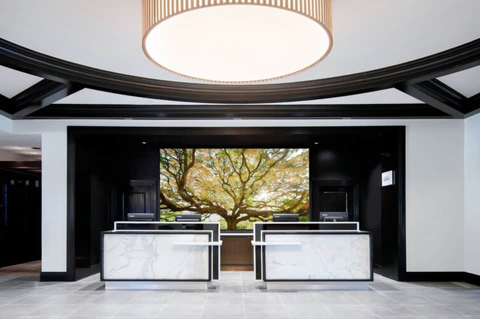 Modern hotel lobby with dual marble reception desks and artistic tree mural