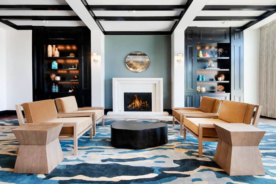 Elegant lounge with fireplace, tan leather seating, blue patterned rug, and built-in shelving