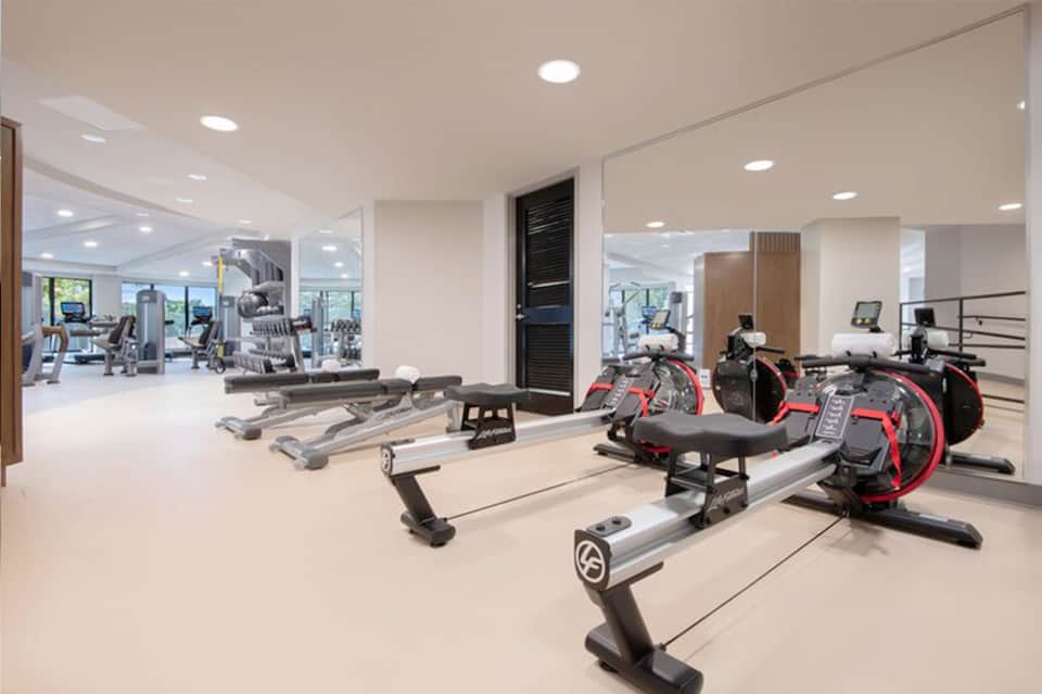 Modern gym with stationary bikes, exercise equipment, mirrors, and large windows overlooking hillside views
