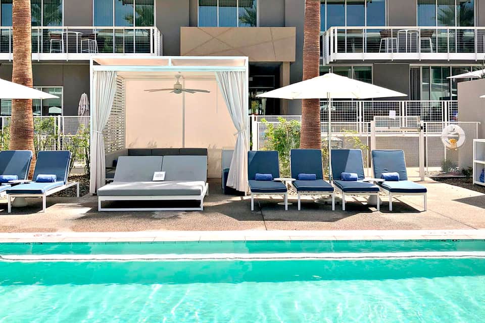 Resort pool area with turquoise water, white loungers, cabana with curtains, and modern building backdrop