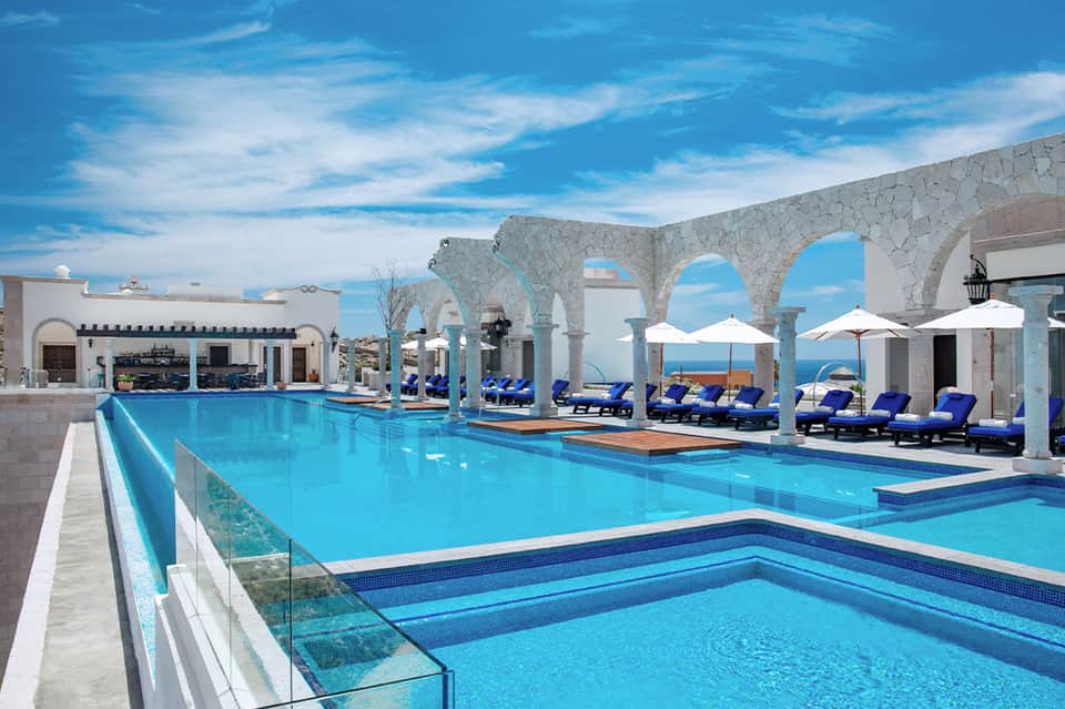 Resort infinity pool with turquoise water, white stone archways, blue lounge chairs, and ocean views