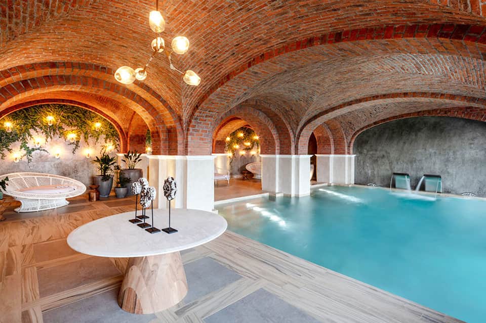 Indoor spa pool beneath ornate brick arches with warm lighting and marble flooring