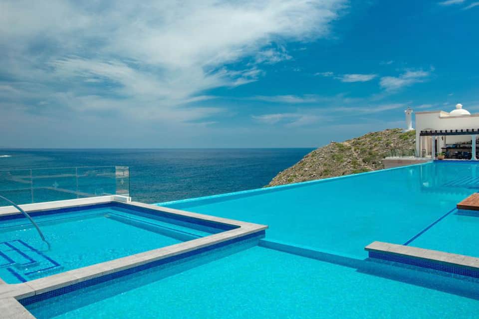 Infinity pool overlooking turquoise ocean and rocky coastline with lighthouse and white building
