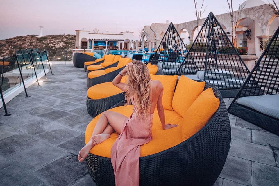 Woman reclining on orange bean bag chair at luxury desert resort with geometric black shade structures