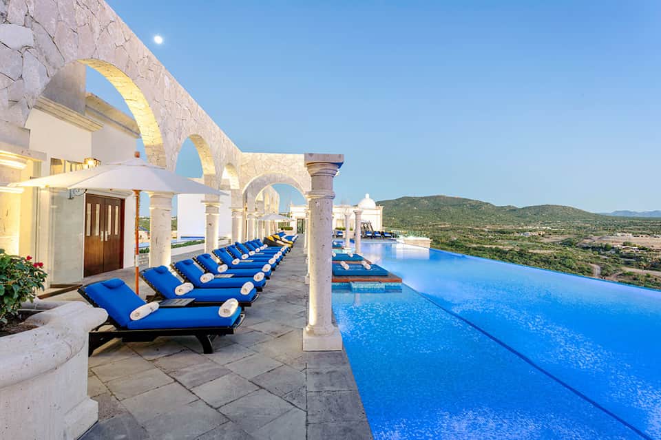 Infinity pool with blue loungers under white arches overlooking desert landscape