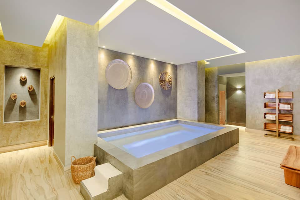 Luxury spa with sunken bathtub, gold-toned walls, decorative plates, and wooden shelving