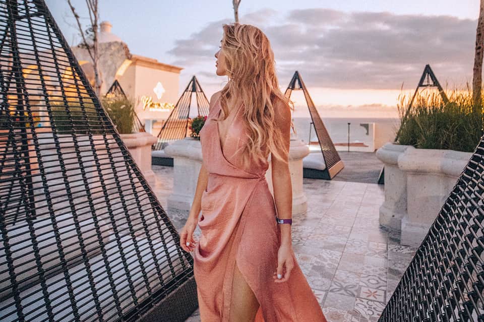Woman in pink dress standing on rooftop terrace at sunset with geometric loungers