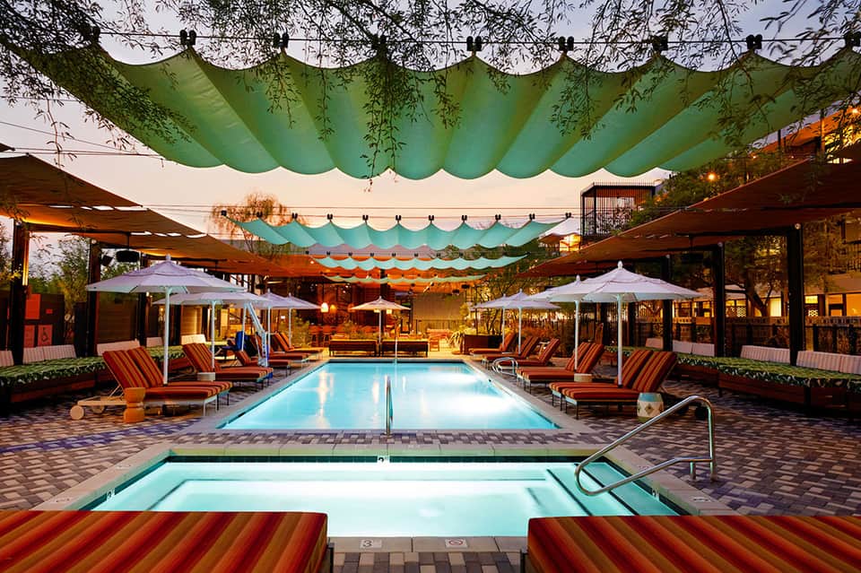 Resort pool deck at dusk with green canopies, loungers, umbrellas, and ambient lighting