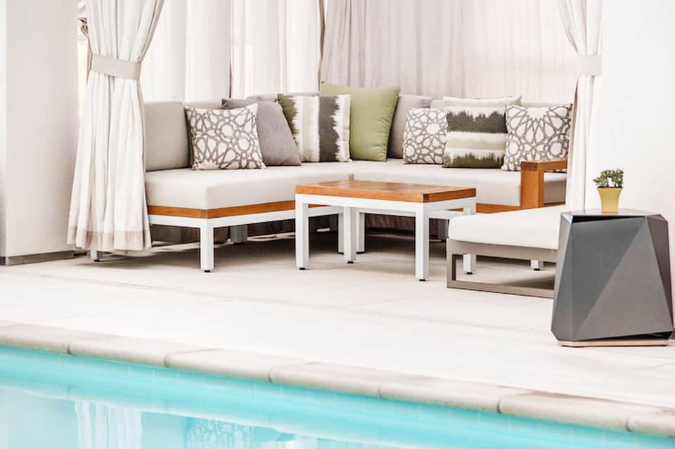 Luxury poolside lounge area with cream seating, decorative pillows, and sheer curtains by turquoise water