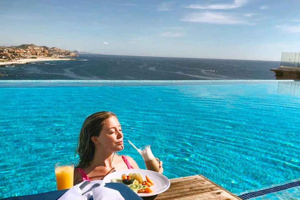 Woman dining by infinity pool overlooking Mediterranean Sea and coastal cliffs