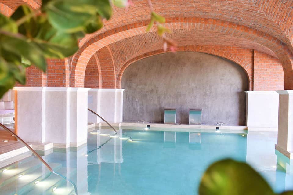 Indoor spa pool with turquoise water beneath red brick arches and white privacy partitions