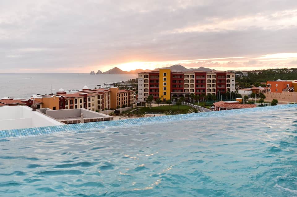 Beachfront resort at sunset with colorful buildings, infinity pool, and rocky coastal landscape