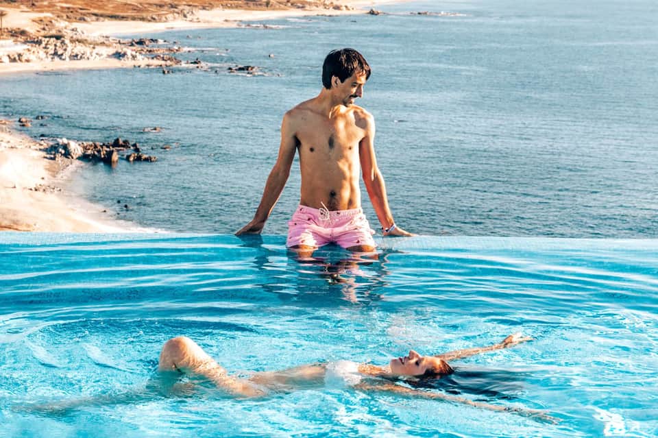 Guests swimming in infinity pool with ocean and rocky coastline backdrop