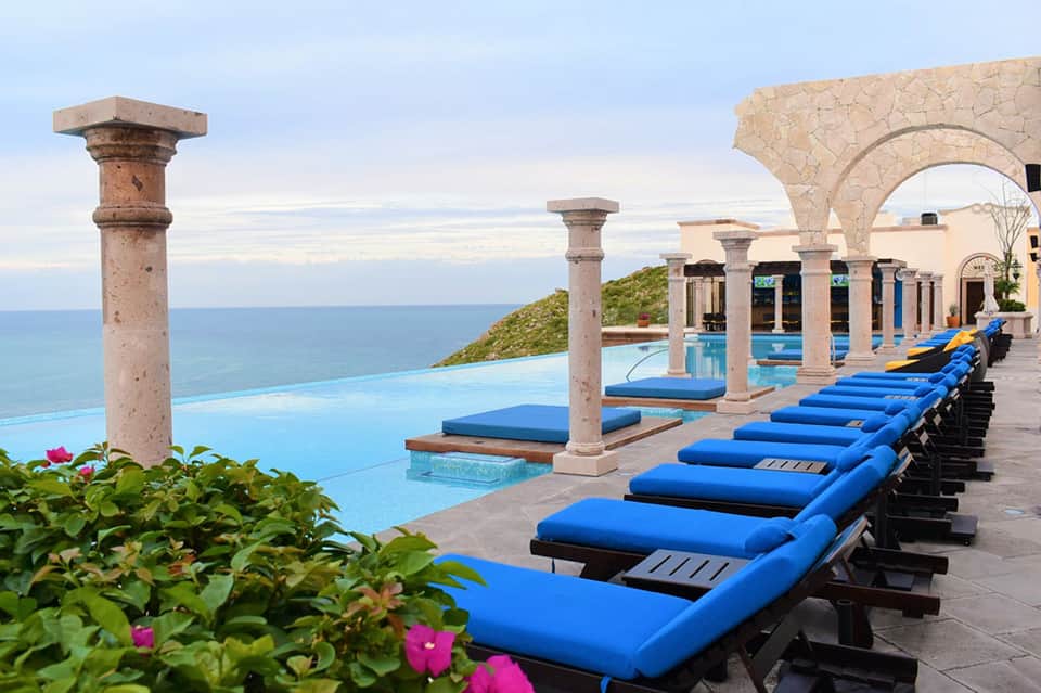 Cliffside infinity pool with blue loungers, Mediterranean columns, and ocean views