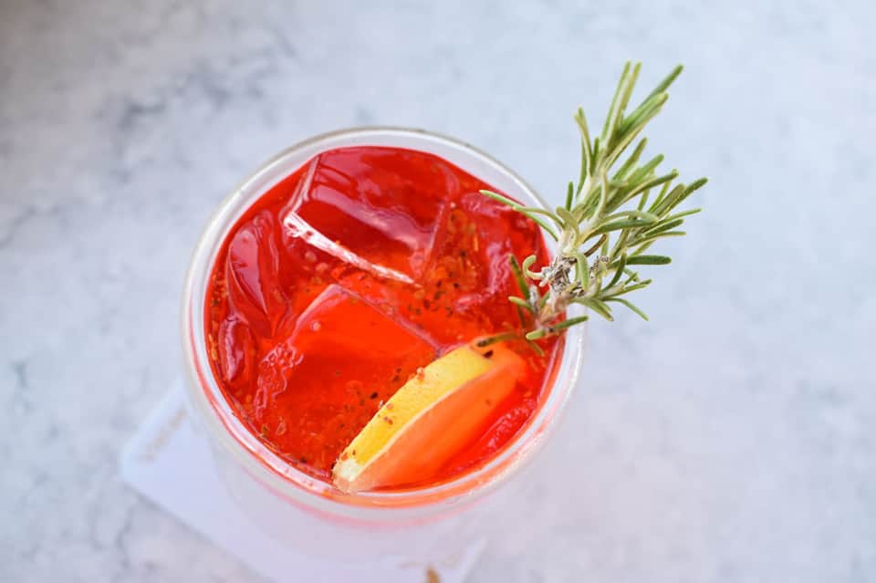 Overhead view of red cocktail with ice, rosemary sprig, and citrus slice