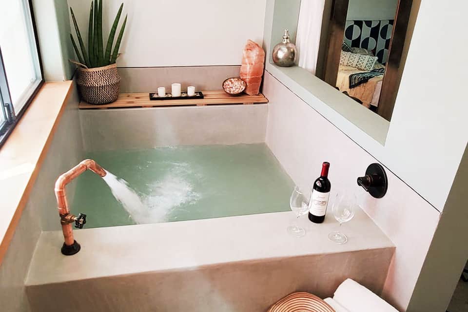Spa-style soaking tub with green water, candlelight, wine bottle, and relaxation amenities