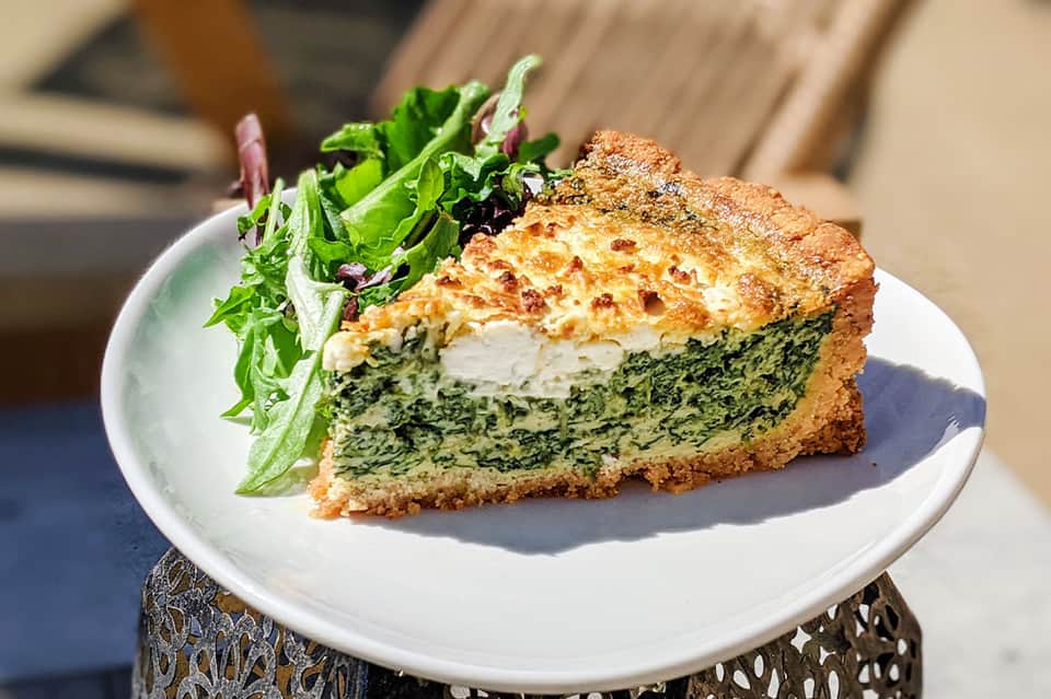 Spinach and cheese quiche slice with fresh salad on white plate by the pool