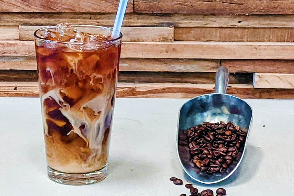 Iced coffee drink next to scoop of roasted coffee beans on wooden surface