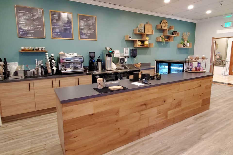 Bright cafe counter with teal walls, wooden cabinetry, menu boards, and espresso machine setup