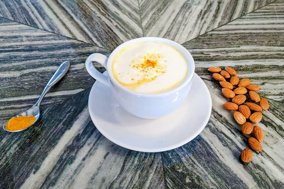 White coffee cup with latte art and almonds on palm leaf patterned surface with spoon