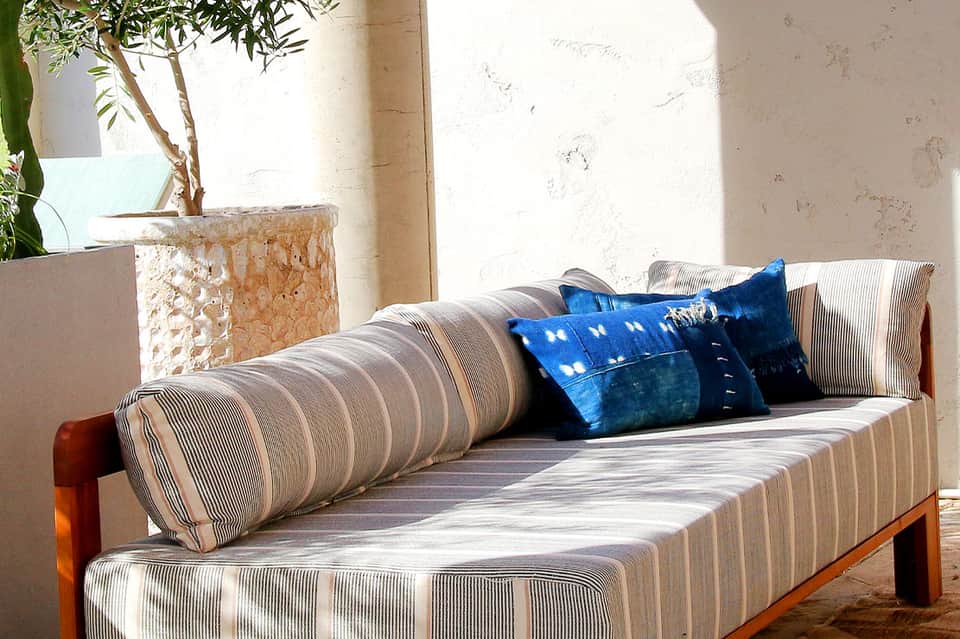 Striped outdoor daybed with blue pillows on a sunlit terrace with potted plant