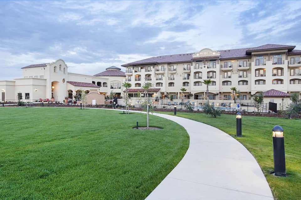 Luxury resort exterior with manicured lawn, curved pathway, and multi-story building