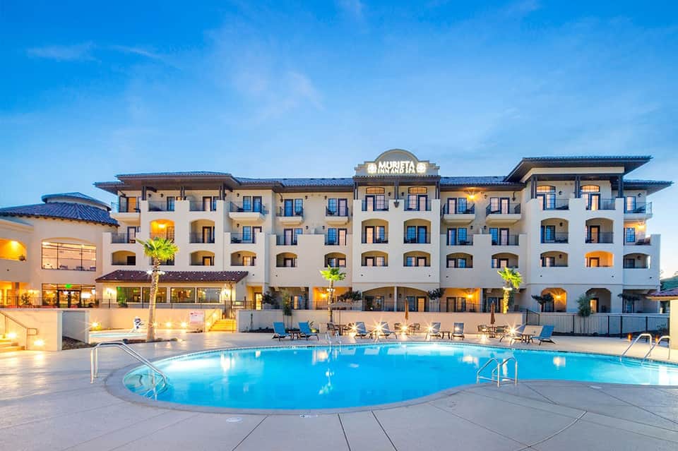 Resort hotel with illuminated pool at dusk, white building facade, blue lighting