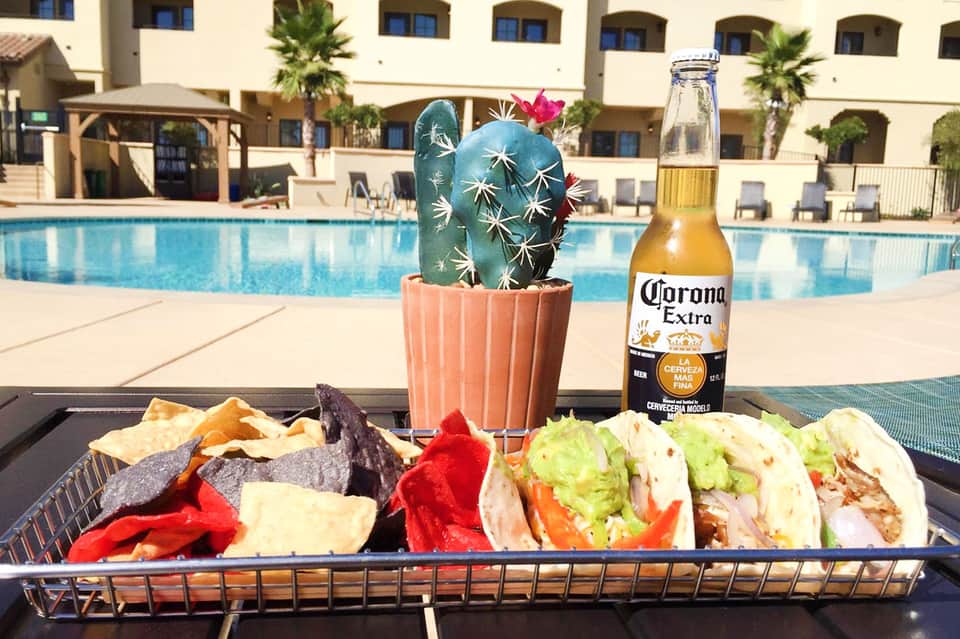Poolside table with tacos, Corona beer, and potted cactus overlooking resort courtyard