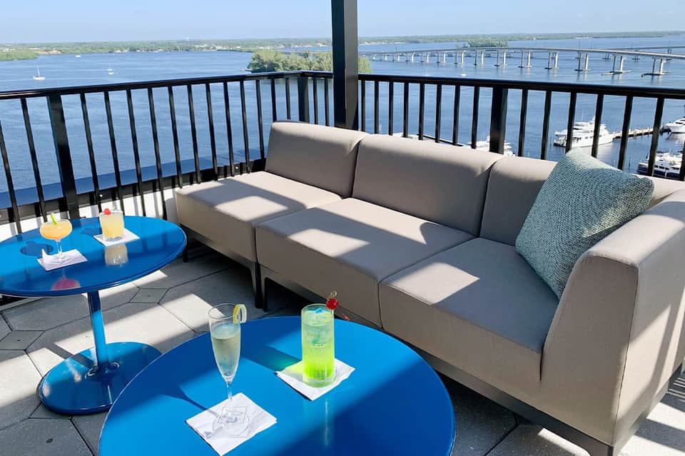 Waterfront balcony with gray upholstered sofa, blue side tables, and bridge views over water