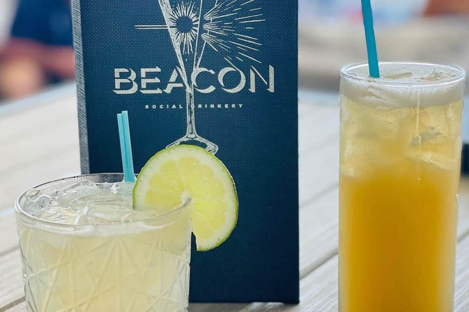 Beacon Social Drinkery logo on napkin with two refreshing citrus cocktails on wooden deck