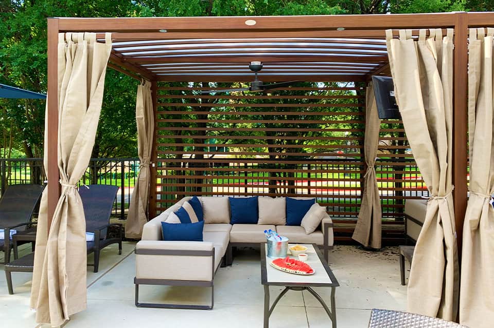 Modern pergola with cream curtains sheltering sectional sofa and coffee table on patio