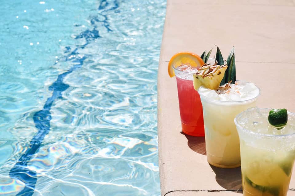 Colorful cocktails on pool deck with blue water and tropical garnishes