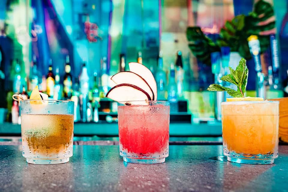 Colorful cocktails on bar counter with citrus garnishes and tropical backdrop