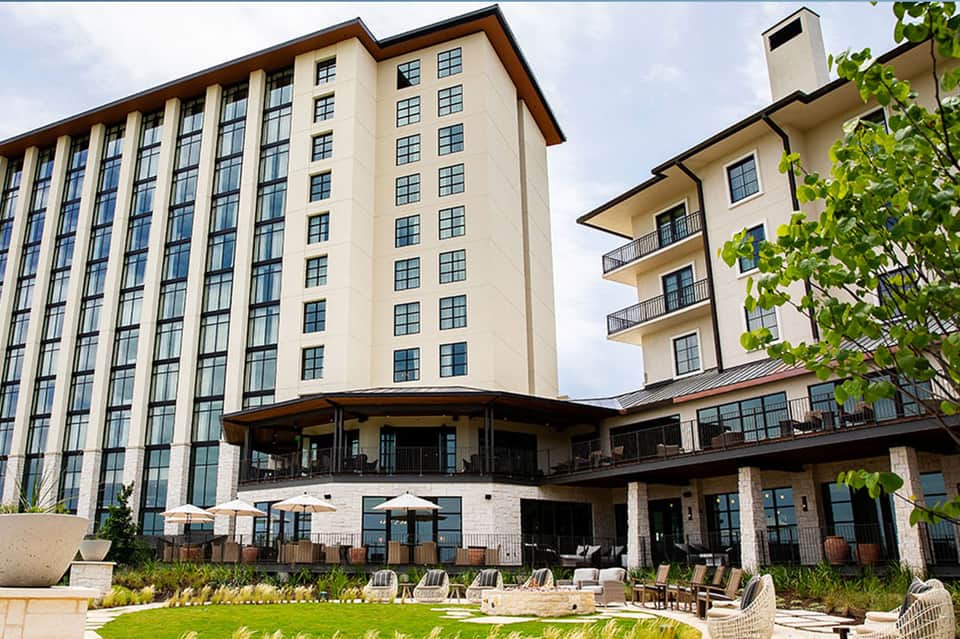 Modern hotel exterior with multi-story building, ground-level terrace, and manicured lawn